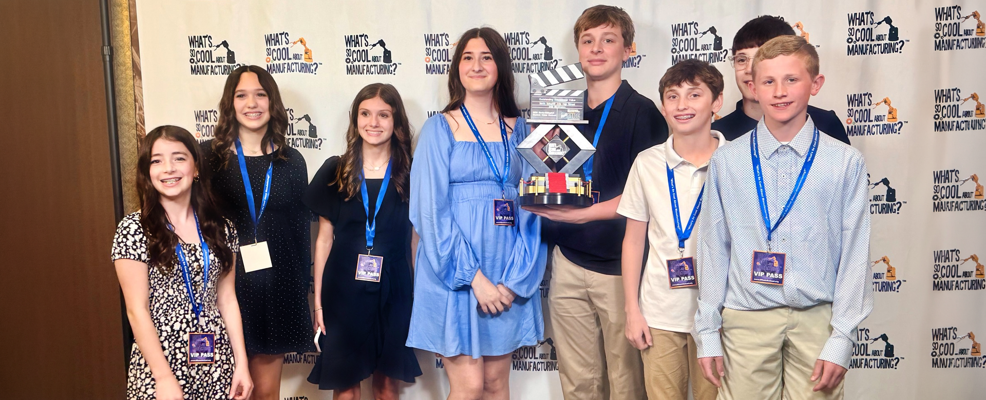 Eight students pose together with a trophy at a “What’s So Cool About Manufacturing?” event.