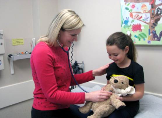 Dr. Allison Ray uses a stethoscope on a young patient's stuffed animal during a pediatric exam.