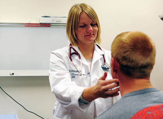 Dr. Amy Wetzel Doolan examines a patient in a clinical setting while wearing her white medical coat.