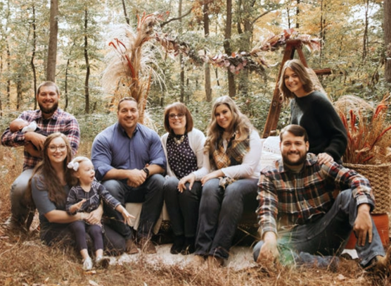 Ed Tarantelli poses with multiple generations of his family in a casual outdoor fall portrait.